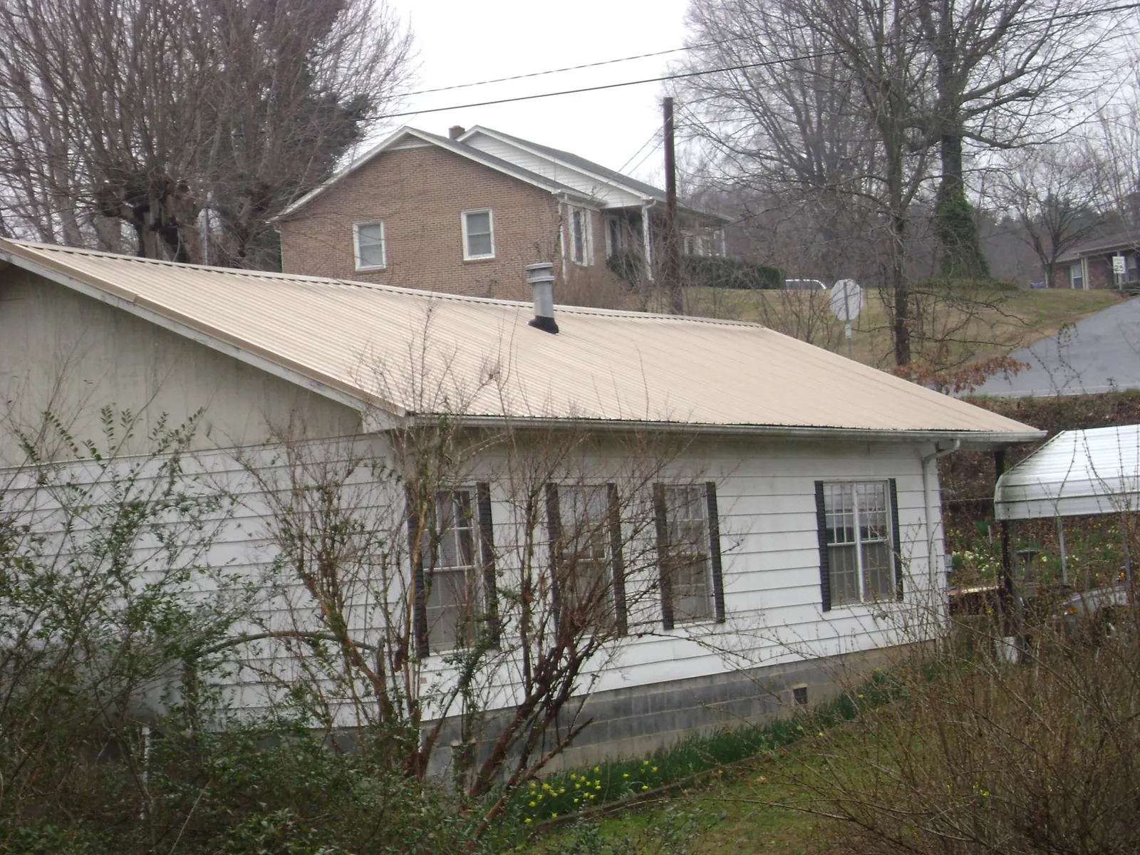 Tan metal roof on a white sided house set into a hillside — Commercial Roofing by Roofing Brothers in Grant